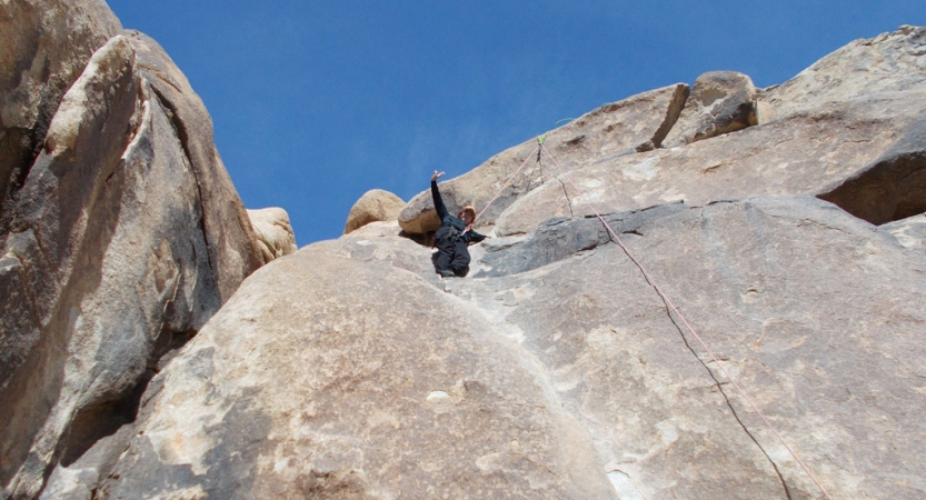 a person wearing safety gear is secured by ropes on a rock wall as they wave to the camera below them